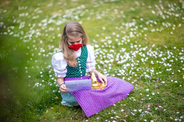 Graz THEMENBILD - Ein Maedchen in Trachtund mit NMS-Maske mit einem Osternest und Schokolade-Hasen auf einer Blumenwiese, aufgenommen am 10. April 2020, in Graz a girl in traditional austrian dress and a face mask is seeking for a easter present in a flower meadow on 10 April 2020.