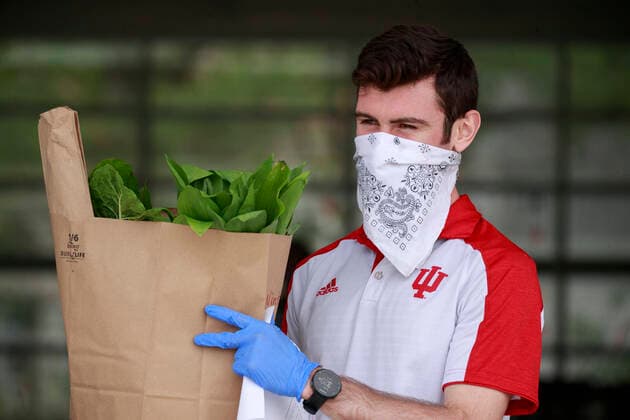 April 11, 2020, Bloomington, Indiana, United States: A man wearing a face mask and gloves and working for the Bloomington Community Farmers Marketm, carries an order to a customer as food is being distributed in a drive-thru arrangement at the Switchyard Pavilion. Bloomington United States - ZUMAs197 20200411_zaa_s197_182 Copyright: xJeremyxHoganx