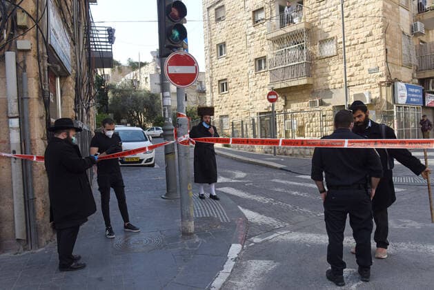 Ultra-Orthodox Jews stand behind police tape, enforcing travel restrictions against the coronavirus, in the Geula religious neighborhood, in Jerusalem, on Sunday, April 12, 2020. The Israeli government deployed a 1,000 police to enforce a full closure on Jewish religious neighborhoods with the highest rate of coronavirus in Jerusalem. According to the Health Ministry about 75 percent of the infected in Jerusalem live in the Ultra-Orthodox neighborhoods.  JER2020041215 DEBBIExHILL