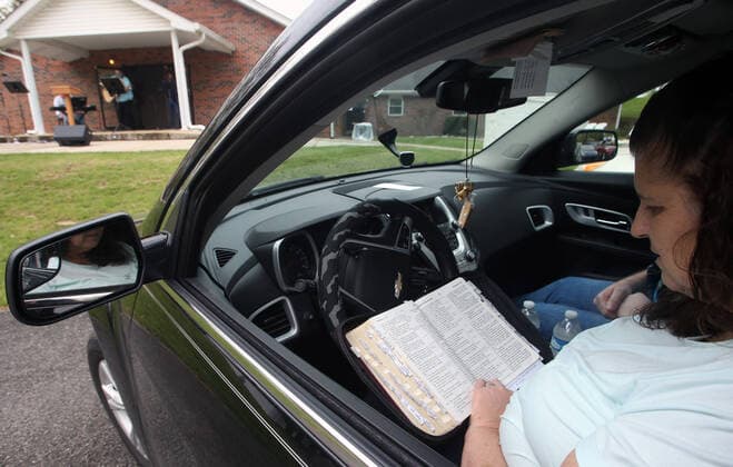 Parishioner Cathy McNary follows a passage from Matthew 1:12 in her Bible from her car during a Easter Sunday service at the Faith Baptist Church in St. Charles, Missouri on Sunday, April 12, 2020. The church held a parking lot service, keeping parishioners in their cars, listening to music and a sermon, honking their horns for approval.  SLP2020041213 BILLxGREENBLATT
