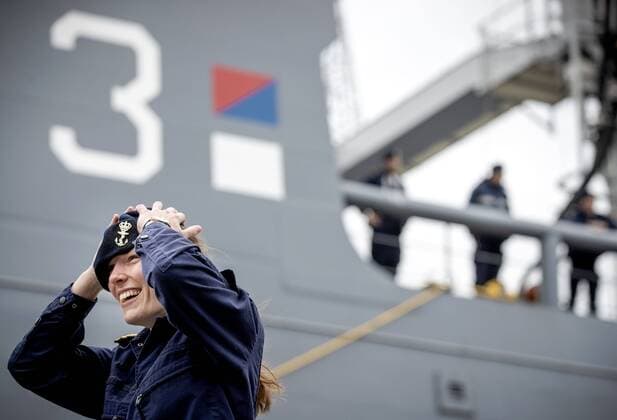2020-04-13 08:46:29 DEN HELDER - Een zeearts van het marineschip Zr.Ms. Karel Doorman houdt haar baret vast tijdens een zware windvlaag voorafgaand aan het vertrek vanuit Den Helder naar het Caribisch Gebied. Defensie zet het schip en de bemanning in ter ondersteuning in de coronacrisis. Het schip blijft er voor minimaal drie maanden aan wal. ANP SEM VAN DER WAL  Copyright: xANPxSEMxVANxDERxWALx x409507430x
