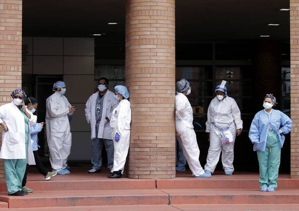 Healthcare workers wearing protective face masks and medical clothes stand outside of an entrance to Wyckoff Heights Medical Center in New York City on Tuesday, April 14, 2020. As of today nearly 285,000 have been infected and more than 14,000 people have died in NY, NJ and CT. There are signs however that the curve is flattening.  NYP20200414119 JOHNxANGELILLO