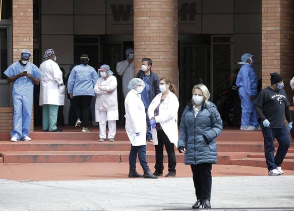 Healthcare workers wearing protective face masks and medical clothes stand outside of an entrance to Wyckoff Heights Medical Center in New York City on Tuesday, April 14, 2020. As of today nearly 285,000 have been infected with Coronavirus and more than 14,000 people have died in NY, NJ and CT. There are signs however that the curve is flattening.  NYP20200414127A JOHNxANGELILLO