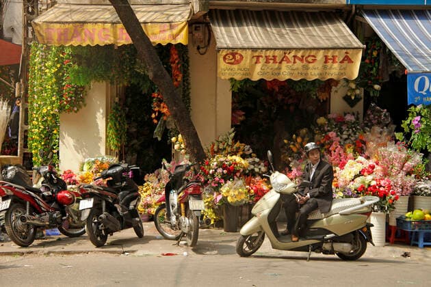 IMAGO Creative: Stadt-Dichotomien Blumenladen junger Vietnamese im Anzug wartet auf seinem Roller vor einem Blumengeschäft in der Altstadt von Hanoi , Vietnam, Asien young men on a scooter waiting in front of a flower store in Hanoi, Vietnam, Asia