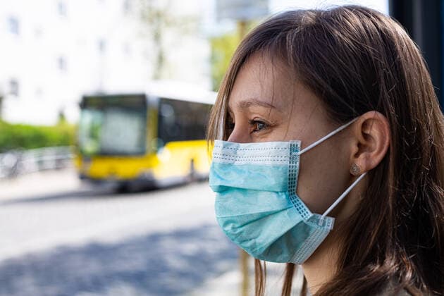 Maskenpflicht im ÖPNV in Berlin, Die Menschen in Berlin müssen ab kommende Woche (27. April) im Öffentlichen Personen-Nahverkehr (ÖPNV) in Bussen, S- und U-Bahnen einen Mund-Nasen-Schutz tragen. Eine Junge Frau steht an einer Bushaltestelle mit einem Mund-Nasen-Schutz. Berlin Berlin Deutschland