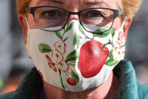 Maskenpflicht in Bayern in allen Geschaeften und im oeffentlichen Personennahverkehr. Masken in allen Variationen gehoeren mittlerweile zum Alltag in Zeiten von Corona. Eine selbstgenaehte,wiederverwendbare Mundschutzmaske,Mundschutz,Mund-Nasen Schutz einer Frau zeigt florale Muster und eine rote Kirsche.