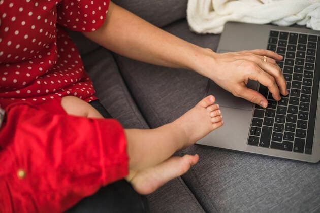 Mother remote working with laptop on sofa while holding her sleepy baby boy model released Symbolfoto FLMF00208