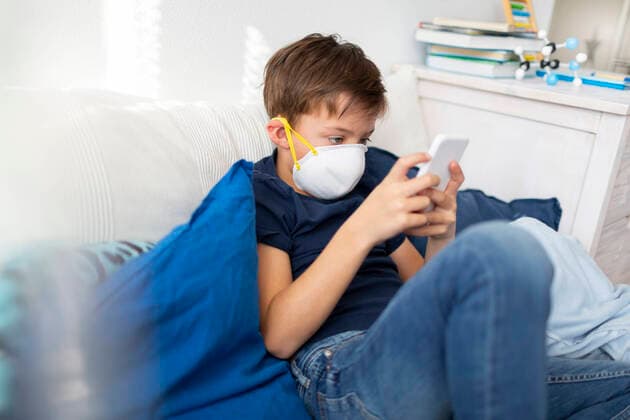 Boy with mask playing with his smartphone during the corona crisis model released Symbolfoto property released HMEF00831