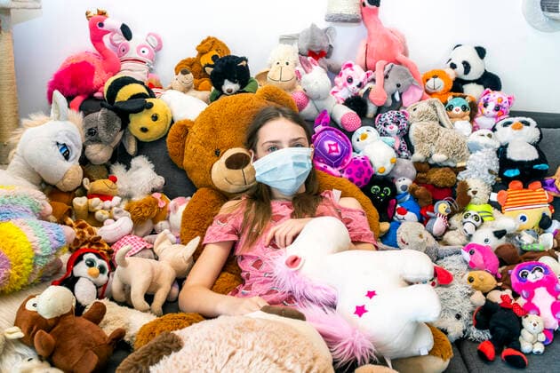 Girl with face mask, sitting on couch, covered in cuddly toys model released Symbolfoto SARF04516