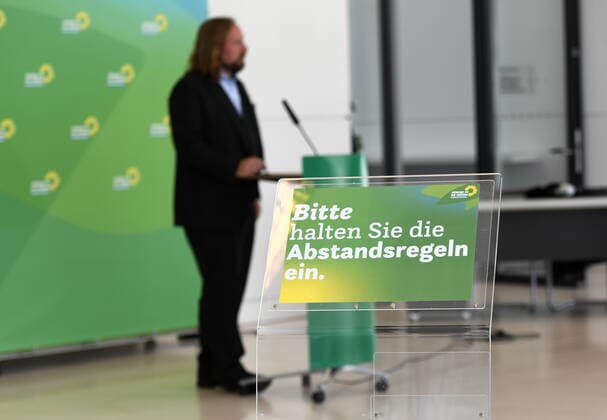 Vor dem Fraktionssaal von Bündnis 90 Die Grünen im Bundestag befindet sich eine Wand mit den Logos der Partei und einem Mikrofon. Dort geben Bundestagsabgeordnete der Partei der Presse Interviews und Statements. Derzeit weißt ein Schild die Medienvertrerter darauf hin, die Abstandsregeln einzuhalten. Im Hintergrund ist der Fraktionsvorsitzende Dr. Anton Hofreiter bei einem Pressestatement zu sehen. Bündnis 90 Die Grünen - Präsentationswand im Bundestag
