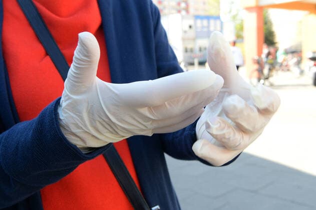 Schutzmasken bald Pflicht beim Einkaufen? -ältere Frau mit Mundschutz zieht sich Handschuhe an MR=YES