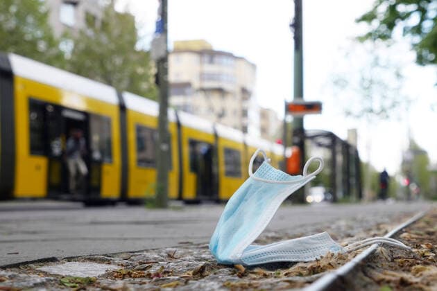 03.05.2020, Berlin - Deutschland. Eine Atemmaske liegt verloren oder weggeworfen auf dem Bürgersteig, eine Straßenbahn erinnert an die Maskenpflicht in öffentlichen Verkehrsmitteln, bei der BVG.
