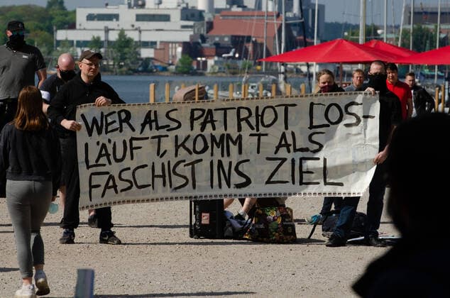 Coronavirus, Demonstration gegen Corona-Maßnahmen Gegendemonstranten halten Transparent vor mit der Aufschrift Wer als Patriot losläuft, kommt als Faschist ins Ziel , am 09.05.2020 in Flensburg, Hafen, Hafenspitze
