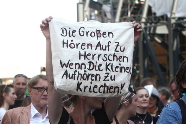 Eine genehmigte Demonstration gegen das coronabedingte Infektionsschutzgesetz und die damit einhergehenden Freiheitsbeschränkungen fand in der Innenstadt von Köln statt, Nordrhein Westfalen, Deutschland. Eine Demonstrantin hält ein Plakat mit Aufschrift die Großen hören auf zu Herrschen, wenn die Kleinen aufhören zu Kriechen hoch.