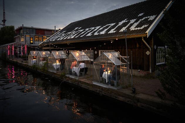 May 12, 2020, Amsterdam, Netherlands: A Dutch restaurant has come up with a way for people to dine in public during the coronavirus pandemic...Eten Restaurant, part of the Mediamatic Biotoop centre in Amsterdam, has tested greenhouse-like booths for customers to eat in, keeping them protected from contracting COVID-19 from other diners...The dining concept is called Serres So pparo es (Separate Greenhouses in English) and allows guests to enjoy a plant-based, four-course meal with a beautiful waterside view of the city...Those who are isolating in household groups (no larger than three) are able to go out together and share a greenhouse...Waiters wear gloves and face shields to try to stop any contamination between staff and diners...Dishes are served on long boards, which can be slid onto the table from outside...They hope to build l - ZUMAc218 20200512_zia_c218_006 Copyright: xCOVERxImagesx