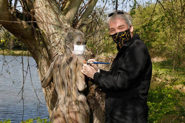 Nature Art Bodypainting mit Model Lisa als Teil eines Baumes an einem Fischeich. Beim Painten wurden Corona-Schutzmaßnahmen getroffen, Model und Künstler Jörg Düsterwald tragen Mundschutz. Springe, 18.05.2020