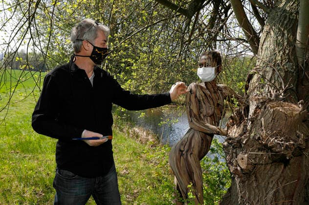 Nature Art Bodypainting mit Model Lisa als Teil eines Baumes an einem Fischeich. Beim Painten wurden Corona-Schutzmaßnahmen getroffen, Model und Künstler Jörg Düsterwald tragen Mundschutz. Springe, 18.05.2020