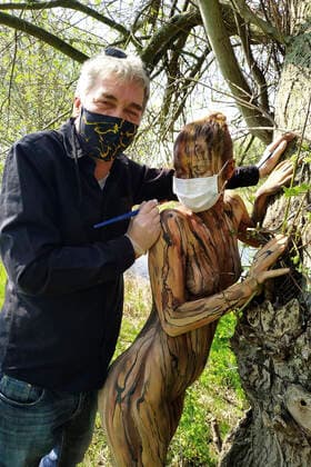 Nature Art Bodypainting mit Model Lisa als Teil eines Baumes an einem Fischeich. Beim Painten wurden Corona-Schutzmaßnahmen getroffen, Model und Künstler Jörg Düsterwald tragen Mundschutz. Springe, 18.05.2020
