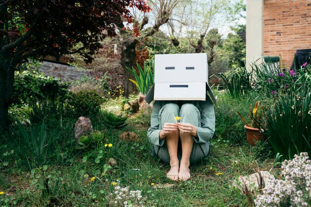 Young woman with cardboard box on her head sitting barefoot in garden model released Symbolfoto AFVF06131