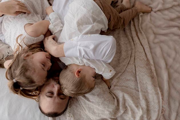 IMAGO Creative: Vaterschaft Father lying on bed cuddling with his two children model released Symbolfoto GMLF00122