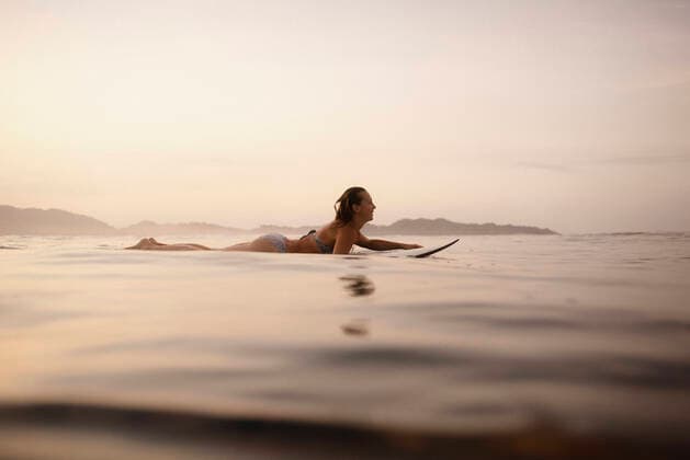 Female surfer lying on surfboard in the evening, Costa Rica model released Symbolfoto HWHF00010