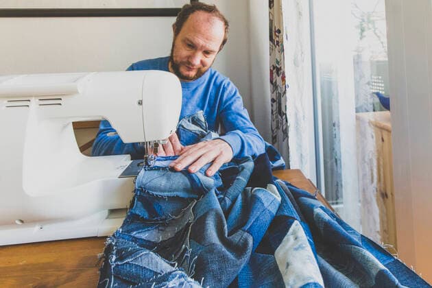 Mature man sewing denim quilt at home model released Symbolfoto property released IHF00336
