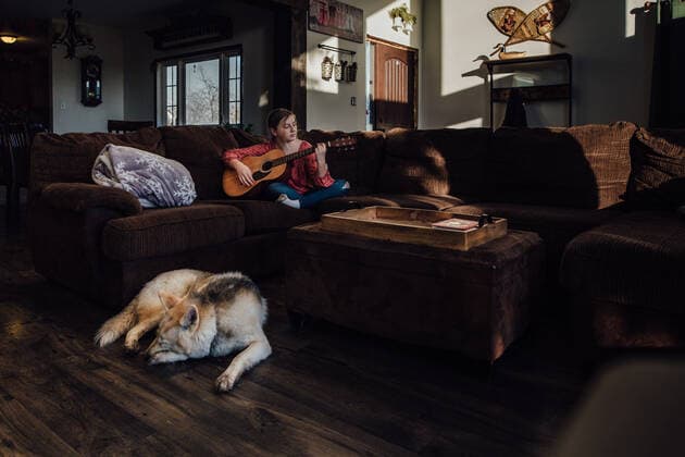 IMAGO Creative: Jahreszeit Winter, Couching Young girl playing guitar on couch with dog sleeping nearby Windsor, ON, Canada CR_JEOH200518-377558-01,model released, Symbolfoto