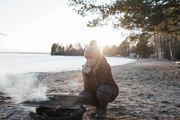 woman warming up by a fire at the beach in winter in Sweden Bjuraker, Gavleborg County, Sweden CR_RABE200331-335629-01,model released, Symbolfoto