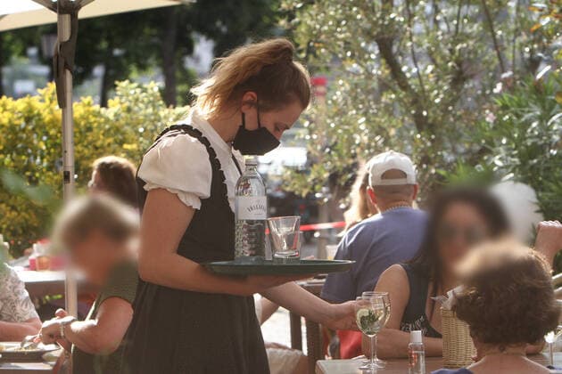 Kellnerin mit Mund- und Nasenschutzmaske bedient Kunden im vollen Außenbereich eines Restaurants in der Innenstadt von Heidelberg, Baden Württemberg, Deutschland *** Waitress with mouth and nose mask serving customers in the full outdoor area of a restaurant in downtown Heidelberg, Baden Württemberg, Germany