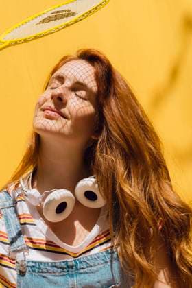IMAGO Creative, Sommer, Schatten-Plätze bei Hitze Relaxed young woman with badminton racket over face wearing headphones around neck during sunny day model released Symbolfoto property released AFVF06451