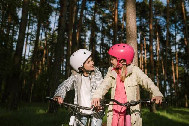 IMAGO Creative: Klimawandel - Umwelterziehung Girl and boy talking while riding bicycles in forest model released Symbolfoto EYAF01084