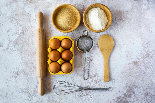 Rolling pin, wire whisk, sieve, chicken eggs, spoon and bowls of flour and brown sugar GIOF08193