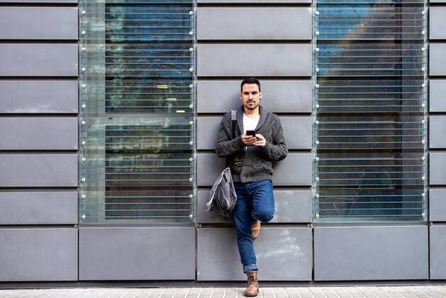 Front view of a bearded man using phone leaning on office building wall Barcelona, CT, Spain CR_RAFE200601A-370953-01 ,model released, Symbolfoto