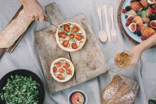 Hands of woman cutting savory pie while friend holding wineglass on table model released Symbolfoto ALBF01253