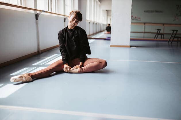 Happy ballet dancer stretching legs on floor in studio model released Symbolfoto property released DAWF01741