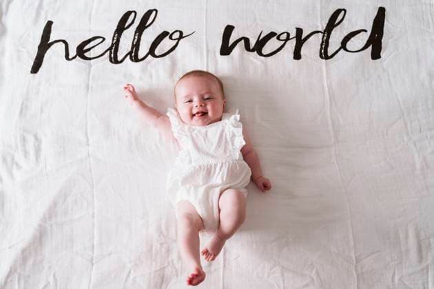 Happy cute baby girl lying on blanket under Hello World text at home model released Symbolfoto EBBF00197