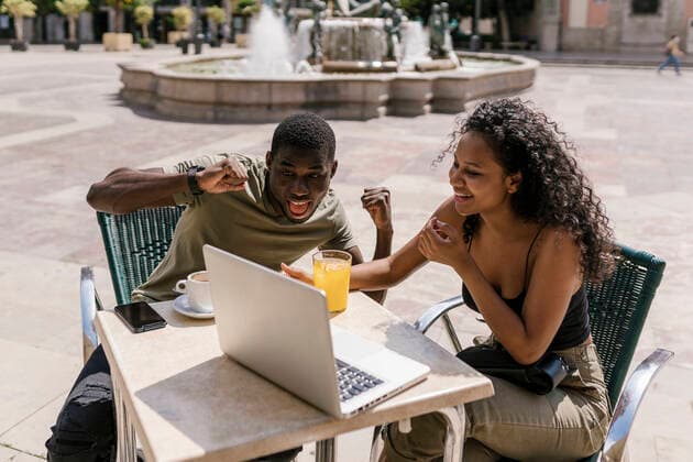 Happy couple gesturing during video call on laptop at sidewalk cafe model released Symbolfoto EGAF00185