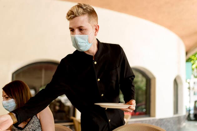 Young waiter wearing protective face mask holding plate while standing by customer in restaurant model released Symbolfoto property released EGAF00205