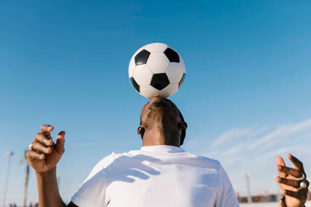 Freizeit Trend: Football Freestyle Close-up of young man balancing soccer ball on head against blue sky model released Symbolfoto EGAF00297