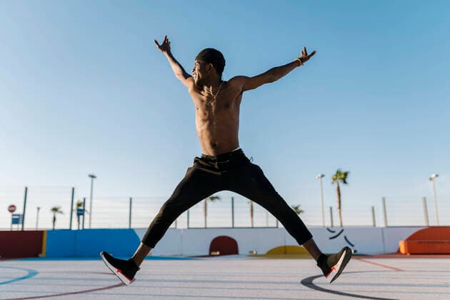 Shirtless young man with arms raised jumping against clear sky in sports court model released Symbolfoto EGAF00303