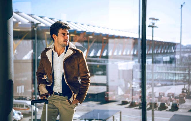 Thoughtful businessman standing with hands in pockets by window at airport departure area model released Symbolfoto EHF00451