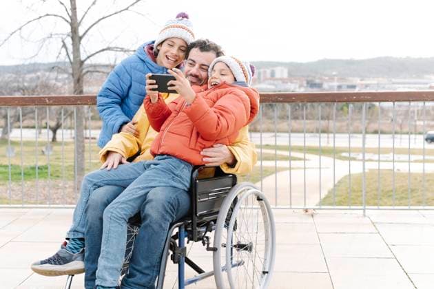 Cheerful boy taking selfie with father and brother on wheelchair in park model released Symbolfoto JCZF00112