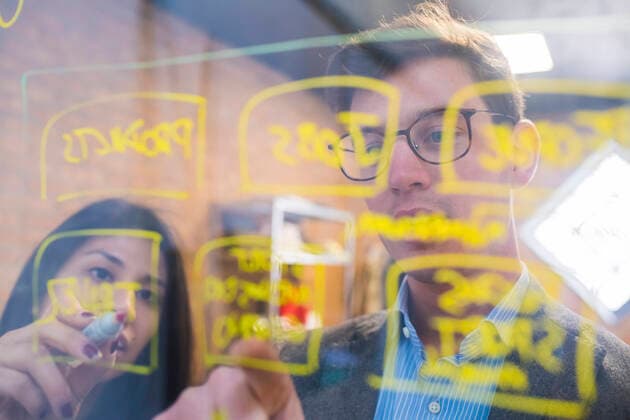 Businessman and woman brainstorming taking notes on glass pane in office model released Symbolfoto property released MEUF00850