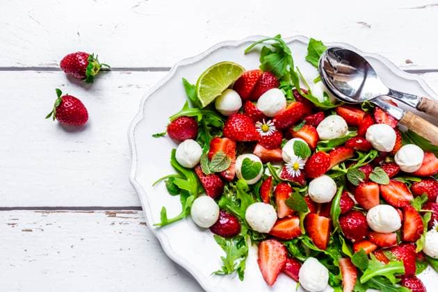 Plate of vegetarian summer salad with lime, arugula, strawberries, mozzarella, mint and daisies SARF04600