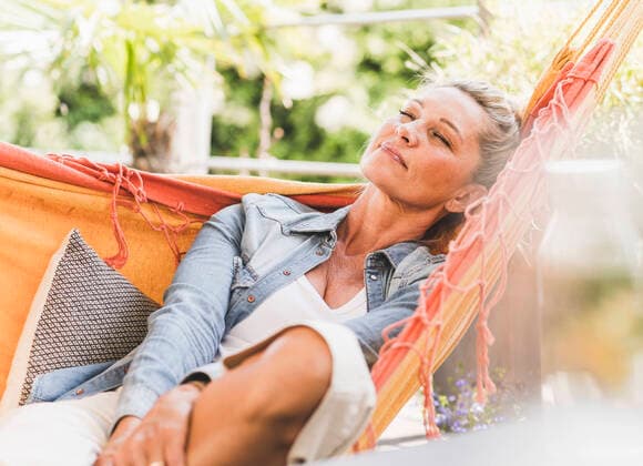 IMAGO Creative: Internationaler Frauenmonat, Gesundheit, Frauen in der Menopause Portrait of mature woman with eyes closed relaxing in hammock on model released Symbolfoto property released UUF20608