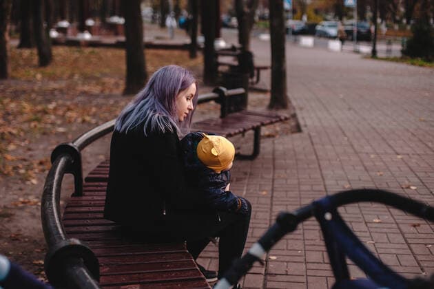 IMAGO Creative: Gesellschaft, Armut Young mother holding baby son while sitting on bench in park CR_DMBE200627-404654-01 ,model released, Symbolfoto