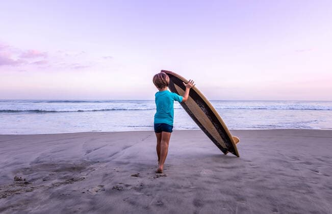 IMAGO Creative: 2022 Farbe des Jahres: Very Peri, Veilchenblau Rear view 4 years old kid carrying a wooden surfboard at the beach São Sebastião, SP, Brazil CR_FRCE200715-452045-01 ,model released, Symbolfoto