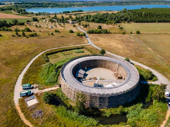 Slawenburg Raddusch am Spreewald DEU Brandenburg Raddusch Â Ende August 2020 öffnet die Slawenburg in Raddusch wieder mit einer neuen, modernen und eindrucksvollen Dauerausstellung zur Archäologie und Geschichte der Niederlausitz. Die Slawenburg Raddusch im Spreewald bei Vetschau zeigt seit 2003 eine Archäologische Dauerausstellung, diese wurde jetzt für rund 2 mio. Euro erneuert. Im Hintergrund der Bischdorfer See, der aus dem Tagebau Seese-Ost entstanden ist. Der Innenraum des acht Meter hohen Walls der Slavenburg wird als Museum genutzt. Das Äussere der Burg wurde wie vor 1000 Jahren mit verkreuzten Holzstämmen versehen und mit einem Gemisch aus Lehm, Stroh und Kuhfladen verschmiert. Der slawische Volksstamm der Lusici, der a