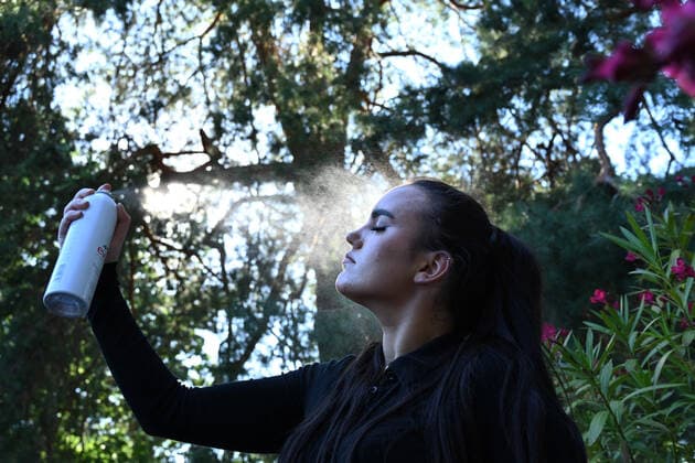 Symbolbild- junge Frau (model released) erfrischt sich mit Wasser-Spray bei hohen Temperaturen