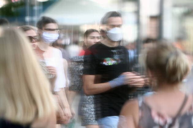 Passanten mit und ohne Mund und Nase Bedeckung spiegeln sich in einer Schaufensterscheibe in der Einkaufsstraße und Fußgängerzone Neuhauser Straße Kaufingerstraße in der Innenstadt von München, Bayern, Deutschland